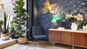 A room with a wooden cabinet, a blue chair, and various potted plants. - Hôtel Henriette (Paris)
