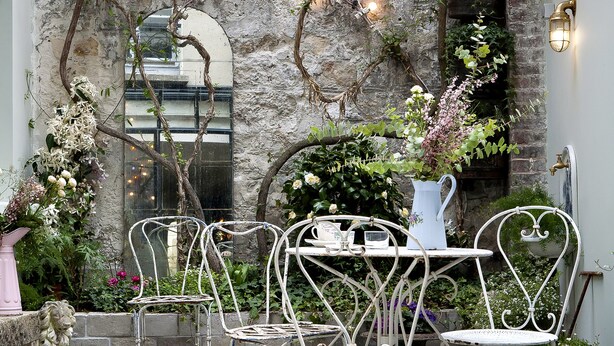 A courtyard with a stone wall, metal chairs, a table, and a vase of flowers. - Hôtel Henriette (Paris)