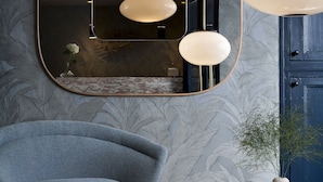 A modern room with a large mirror, a blue armchair, and a wooden table with decorative vases. - Hôtel Henriette (Paris)