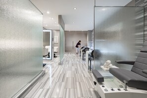 A modern spa room with a marble floor, a massage table, and a glass partition.