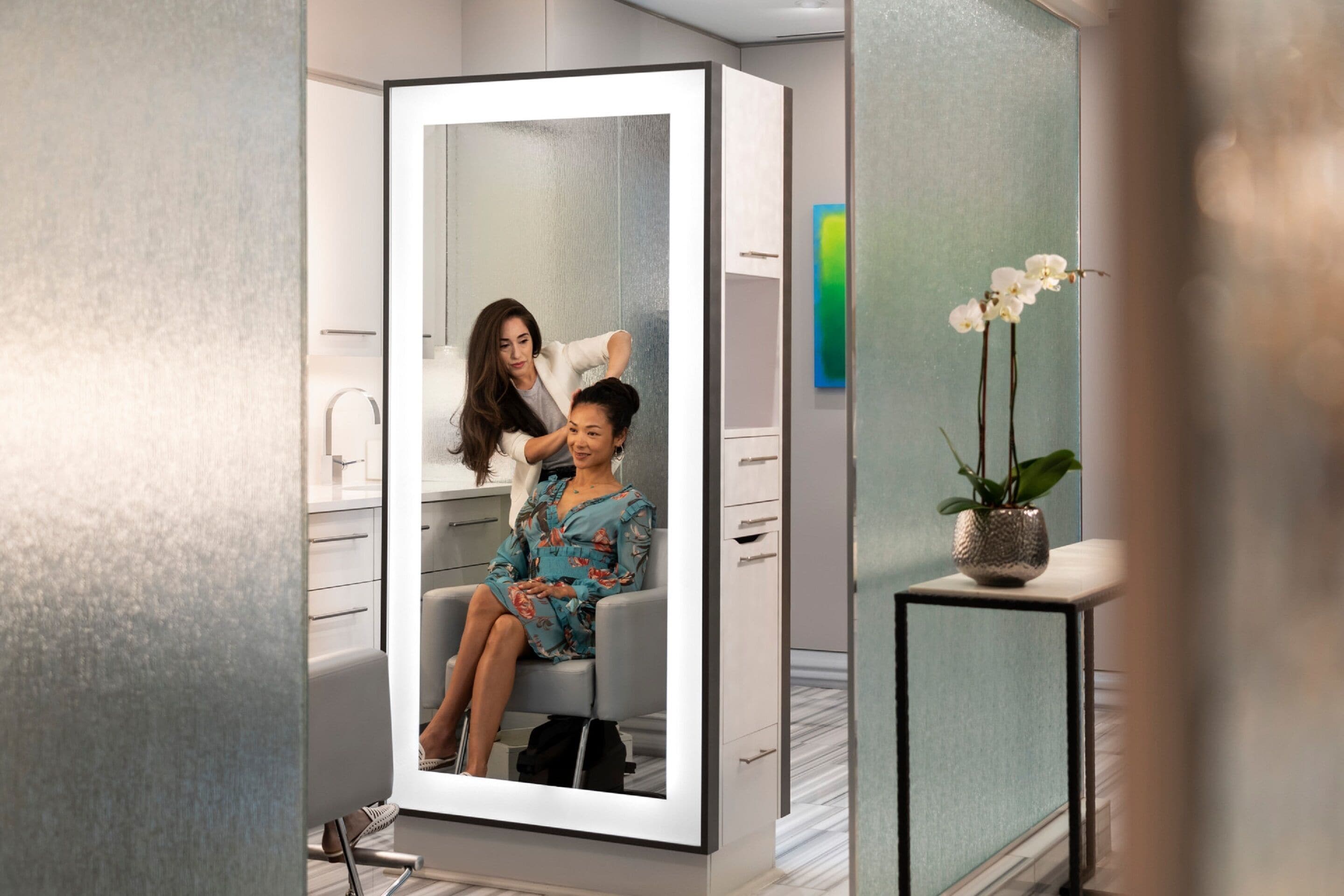 A modern bathroom with a large mirror, a sink, and a potted orchid.