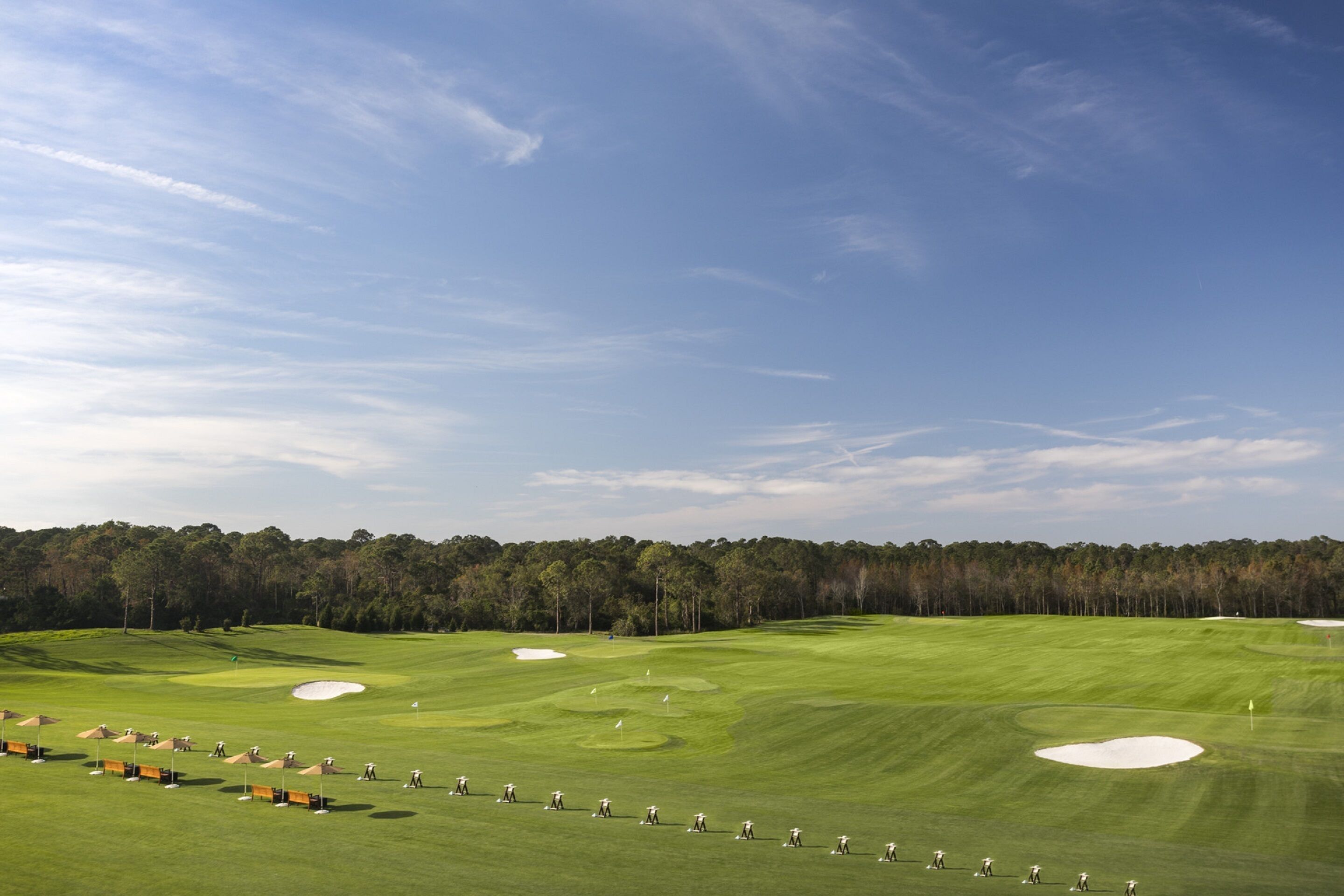 Un parcours de golf avec des bunkers, un ciel dégagé et une forêt en arrière-plan.