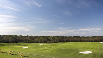 Un parcours de golf avec des bunkers, un ciel dégagé et une forêt en arrière-plan.
