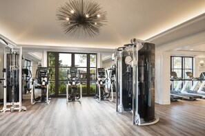 A spacious gym with various exercise machines, large windows, and a modern ceiling design.