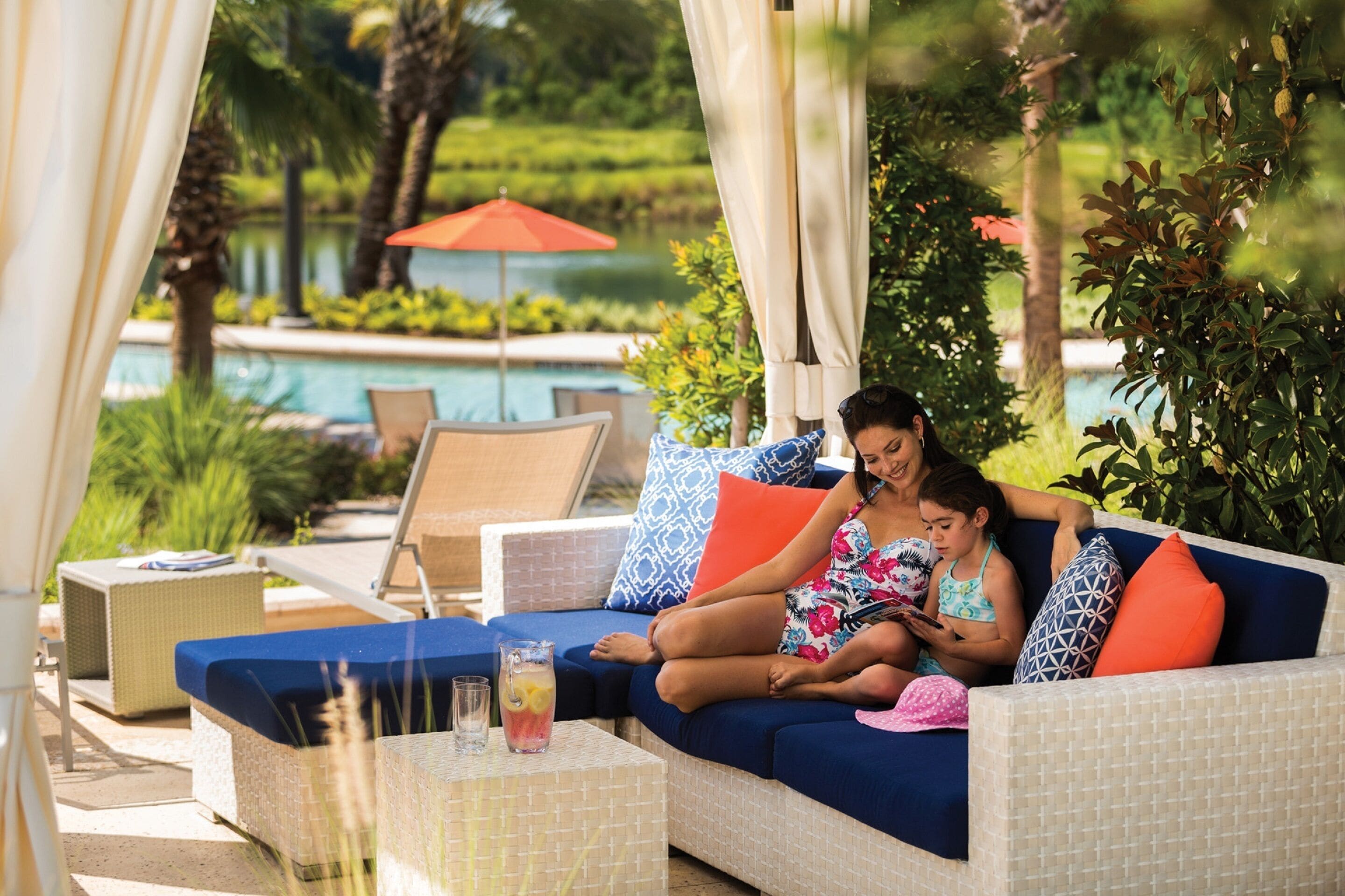 A lounge area with a pool, outdoor seating, and a beverage on a table.