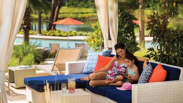 A lounge area with a pool, outdoor seating, and a beverage on a table.