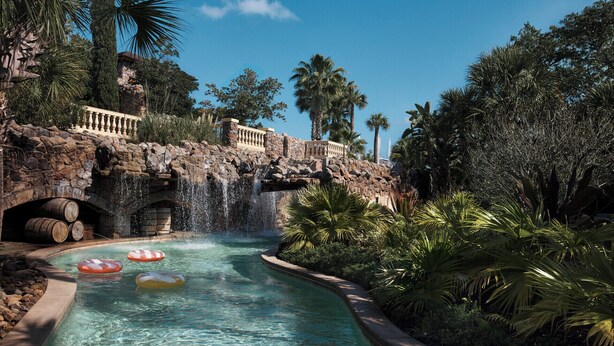 A pool with a waterfall, surrounded by tropical vegetation and a stone bridge. - Four Seasons Resort Orlando at WALT DISNEY WORLD® Resort (Lake Buena Vista)