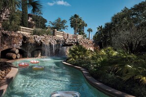 A pool with a waterfall, surrounded by tropical vegetation and a stone bridge. - Four Seasons Resort Orlando at WALT DISNEY WORLD® Resort (Lake Buena Vista)