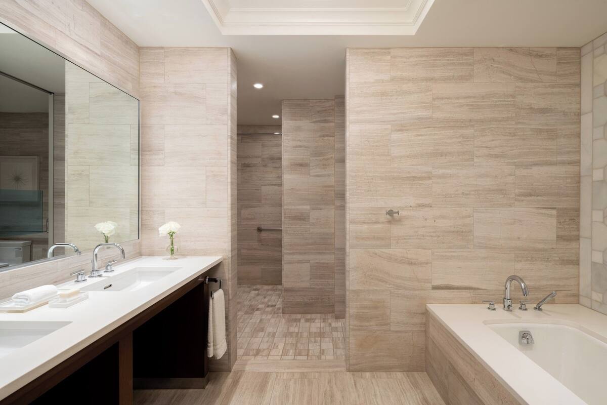 Un baño moderno con un tocador doble, un espejo grande, una bañera y una ducha a ras de suelo con puerta de cristal.