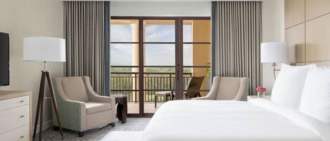 A hotel room with a large bed, two armchairs, a small table, and a balcony with curtains.