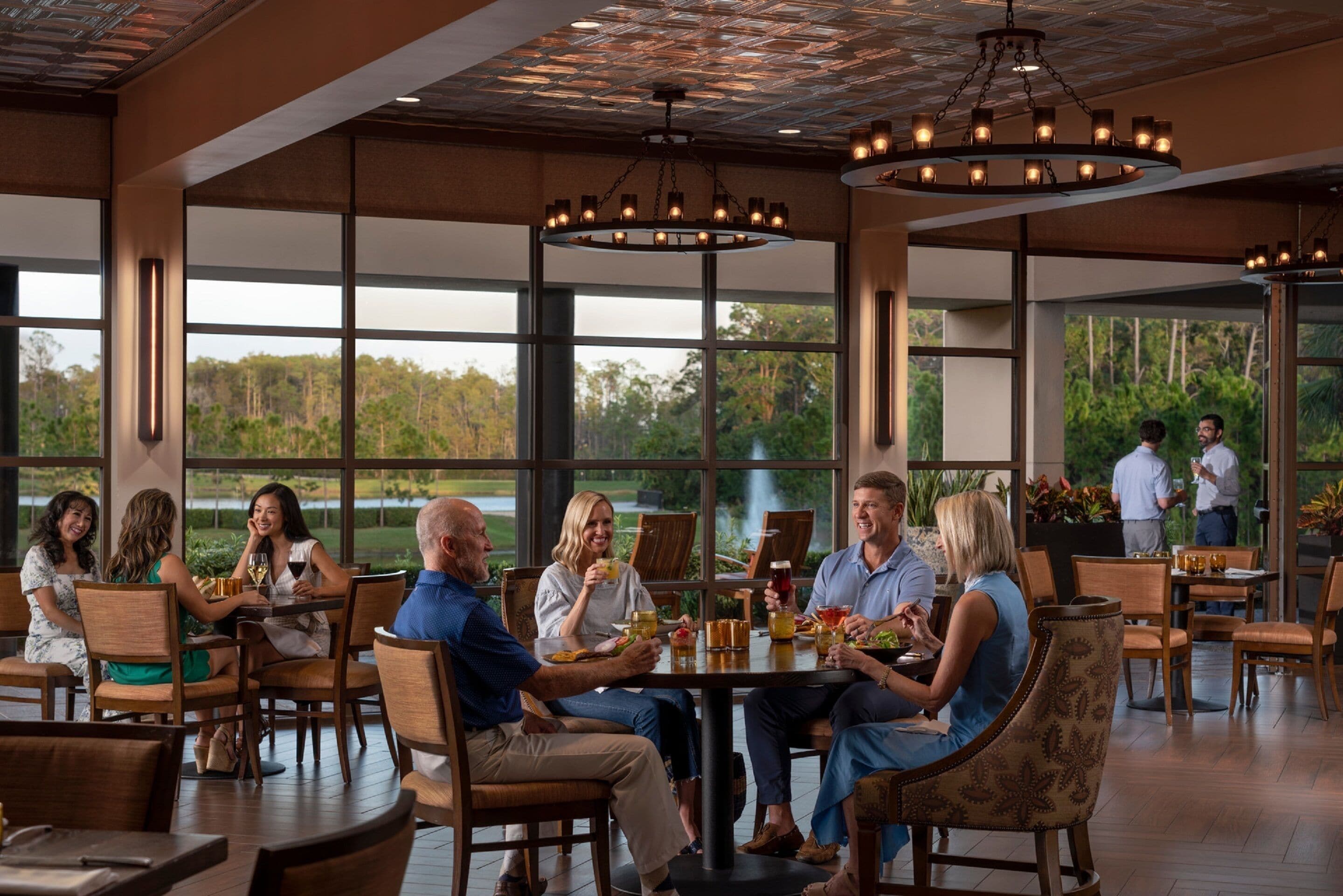 A spacious dining area with large windows, wooden furniture, and a central chandelier.