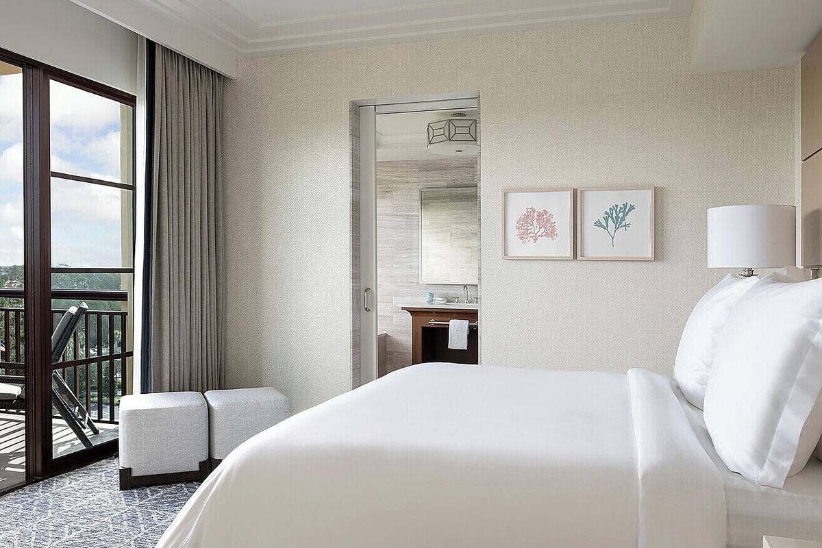 Habitación de hotel con una cama grande, un balcón con vistas, un baño con espejo y obras de arte en la pared.