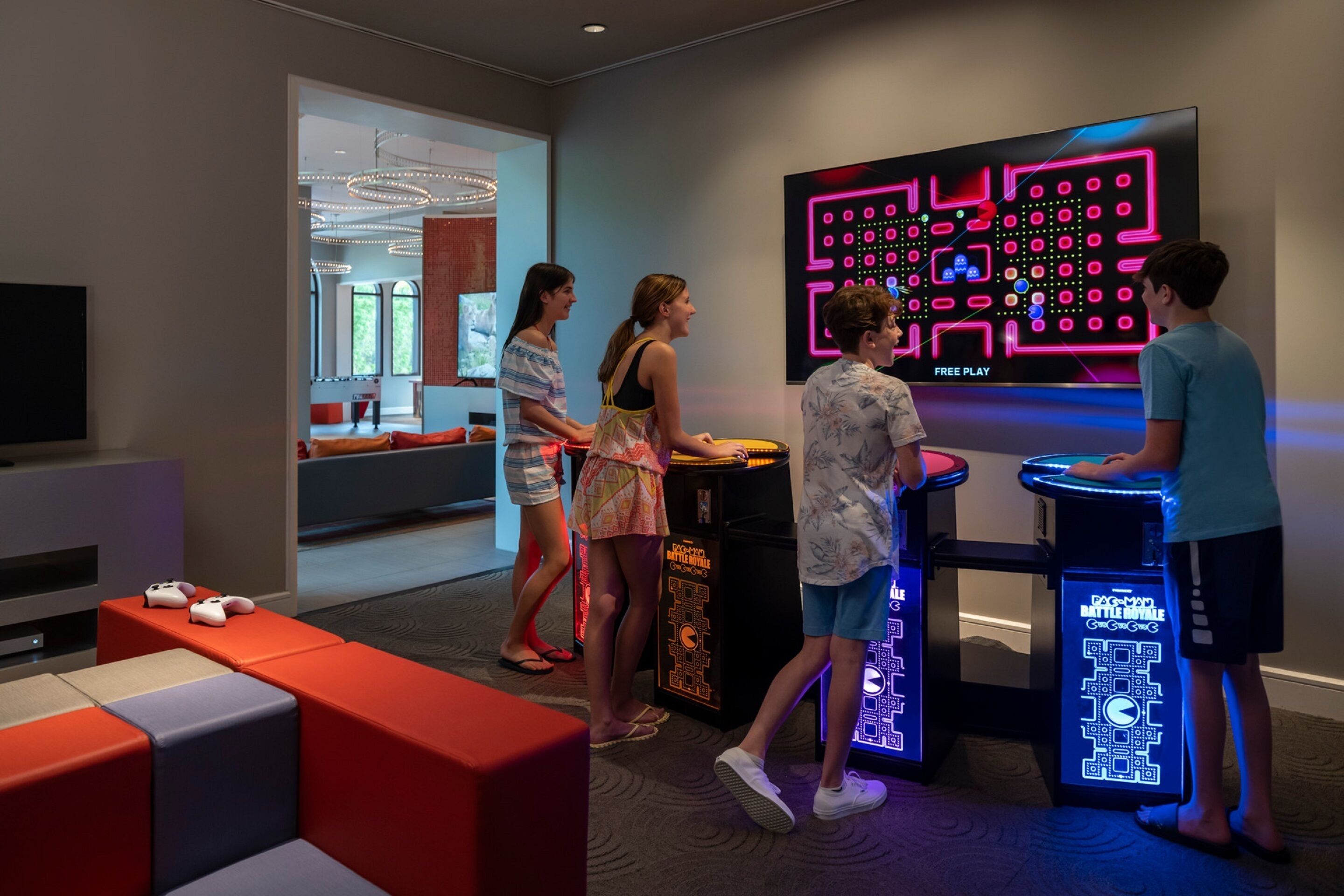Un área de juegos moderna con máquinas de arcade iluminadas con luces de neón y una gran pantalla de televisión.