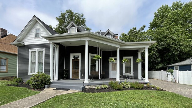 A two-story house with a covered porch, a front door, and a small garden area. - Carriage Lane Inn (Murfreesboro)