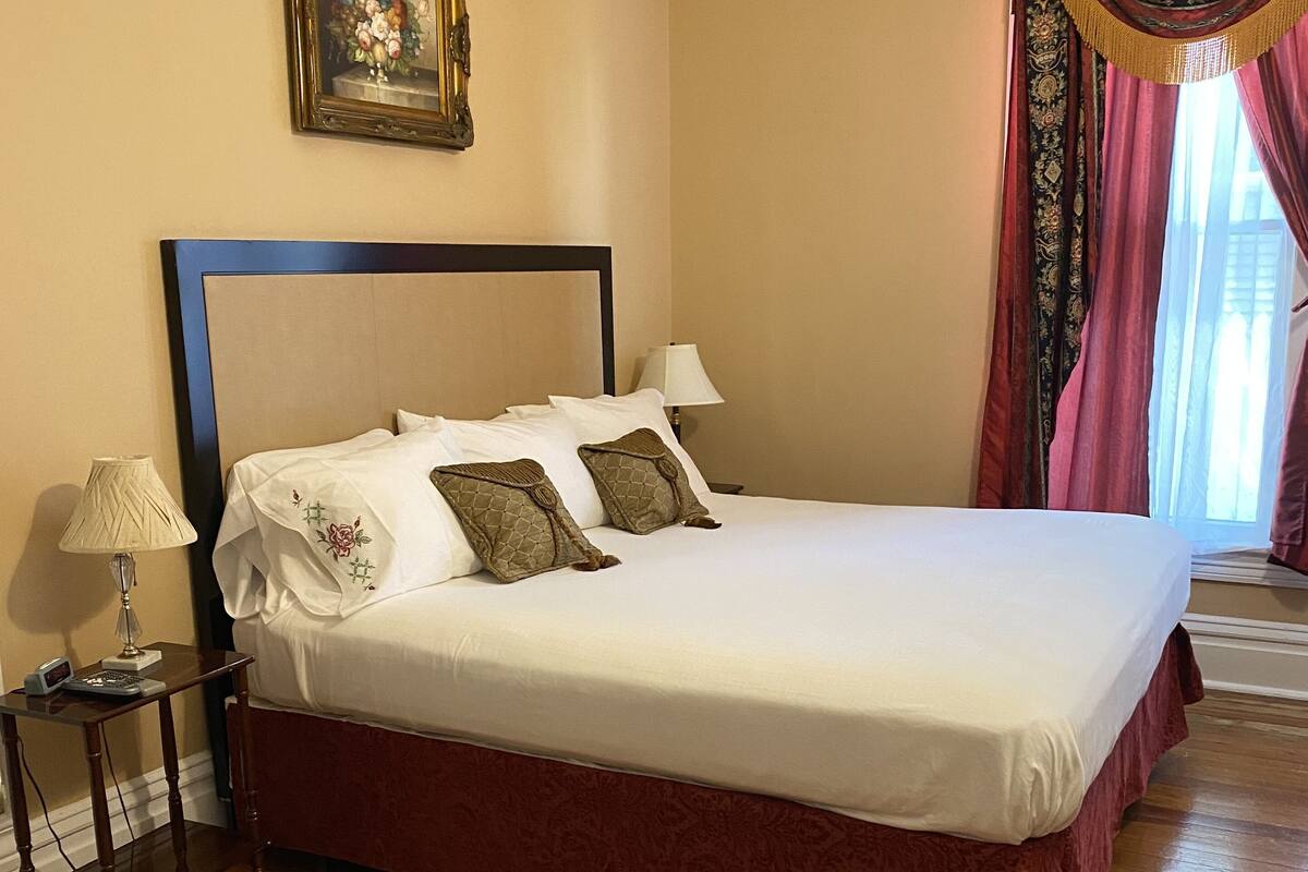 A neatly made bed with white linens and decorative pillows, a bedside table with a lamp, and a framed picture on the wall.