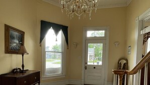 A spacious room with hardwood floors, a chandelier, a door with a window, and a staircase. - Carriage Lane Inn (Murfreesboro)