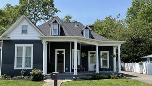 A two-story house with a dark exterior, a front porch with white trim, and a small front yard. - Carriage Lane Inn (Murfreesboro)