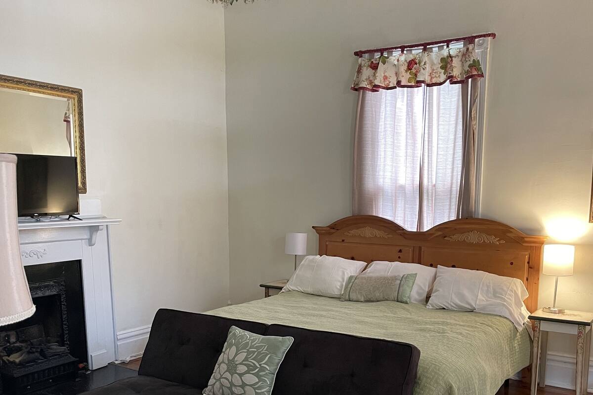 A bedroom with a bed, a sofa, a fireplace, a nightstand, and a mirror.