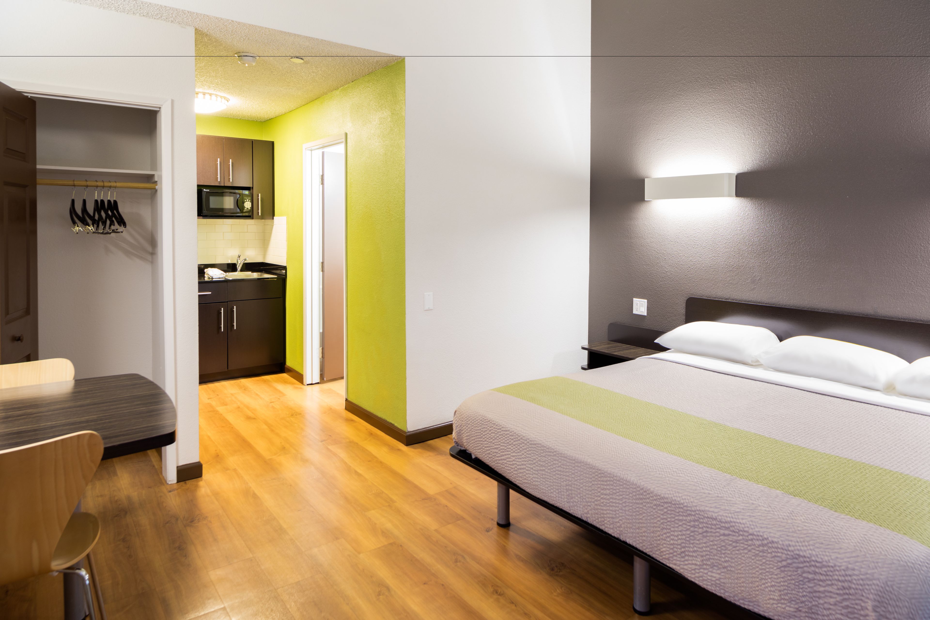 A hotel room with a bed, a desk, a chair, a wardrobe, and a kitchenette.
