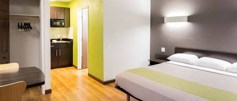 A hotel room with a bed, a desk, a chair, a wardrobe, and a kitchenette.
