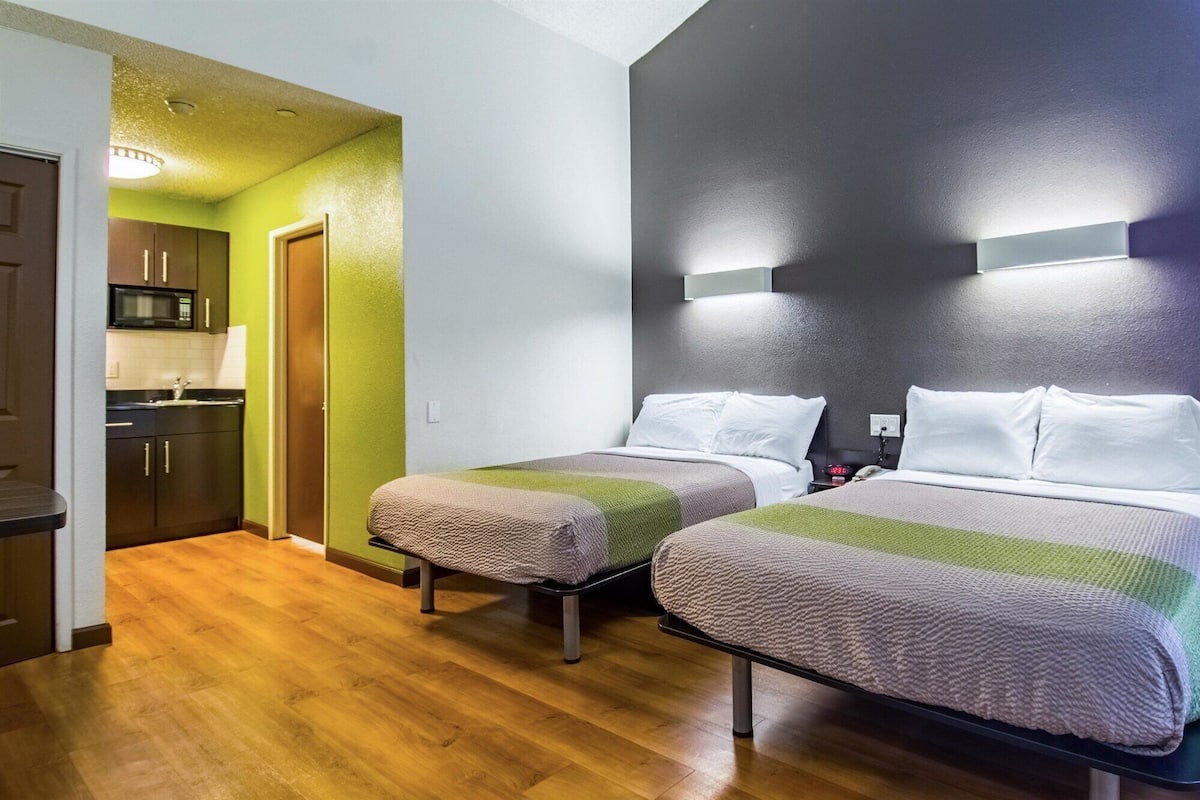 A hotel room with two beds, a kitchenette, and a wooden floor.