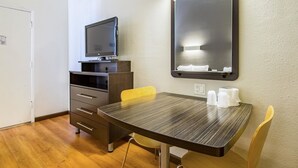A hotel room with a wooden desk, a flat-screen TV, a mirror, and a chair. - Studio 6 Cypress, CA (Cypress)