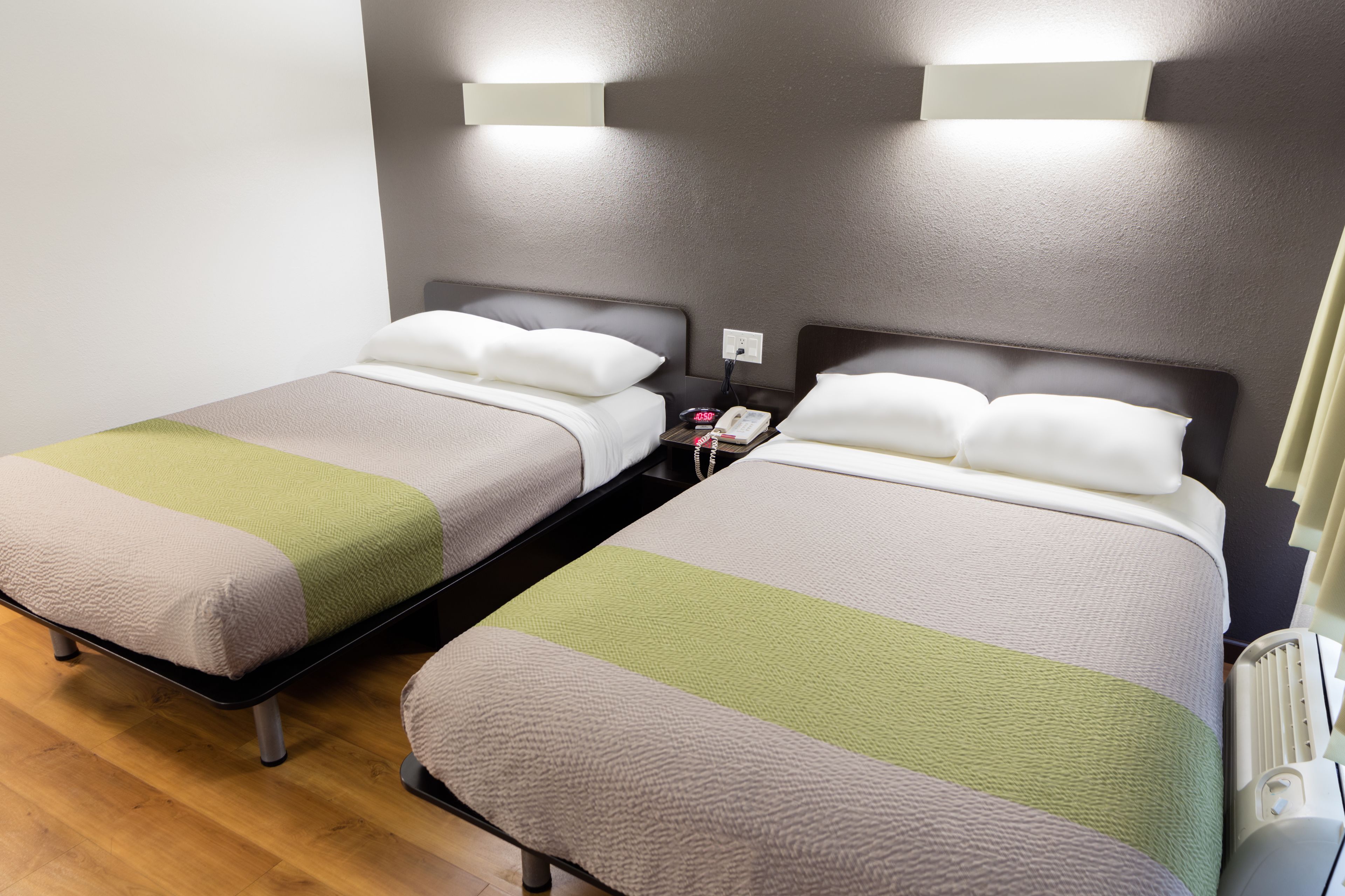 Camera d'albergo con due letti, ciascuno con coperta verde e bianca, un comodino con telefono e lampada, e un termosifone sul lato destro.