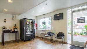 A reception area with a vending machine, a clock, and a television on the wall. - Studio 6 Cypress, CA (Cypress)
