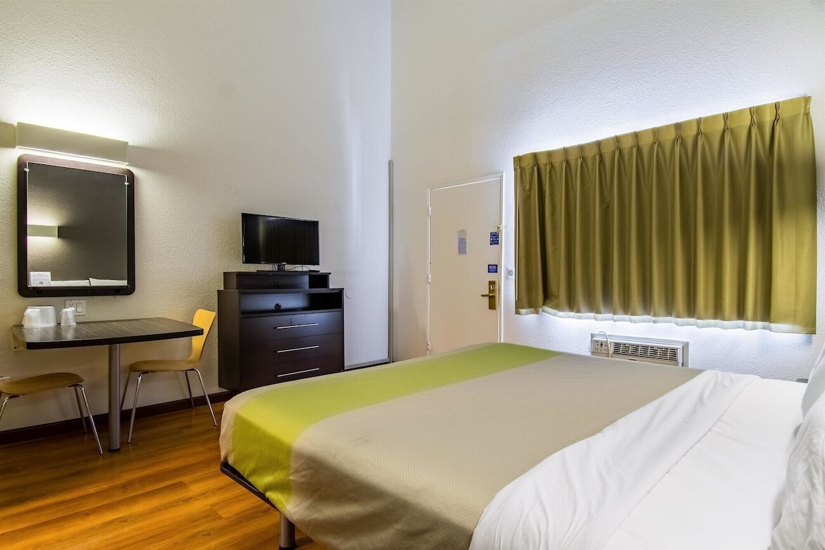 A hotel room with a bed, a desk, a chair, a television, and a window with curtains.