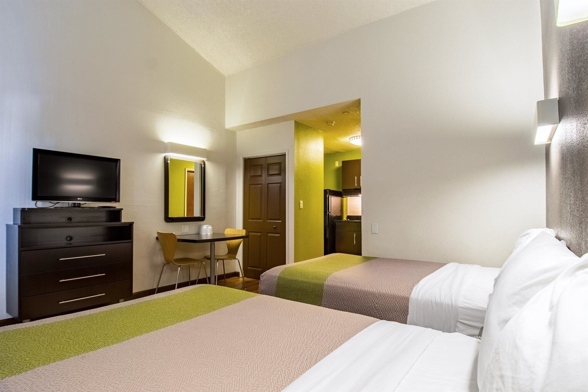 Habitación de hotel con dos camas, un escritorio con silla, televisión, cómoda y espejo.