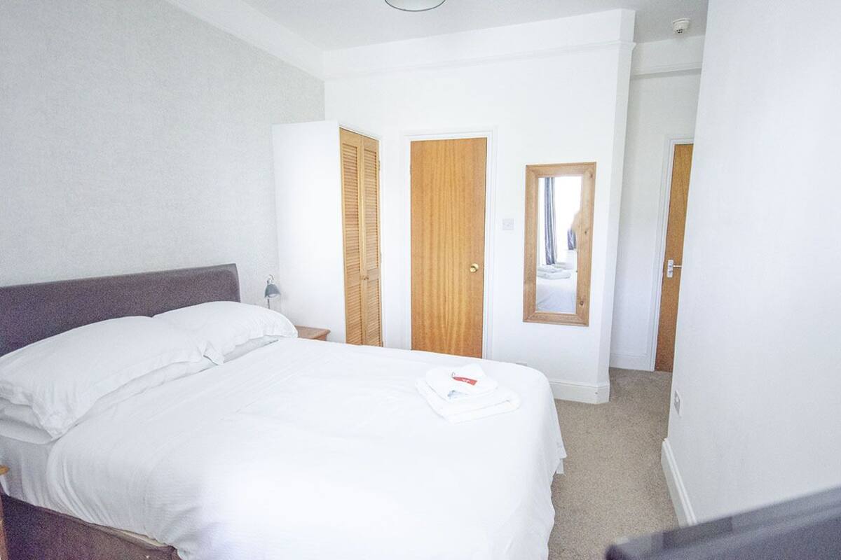 A hotel room with a large bed, a nightstand, a wooden door, and a mirror.