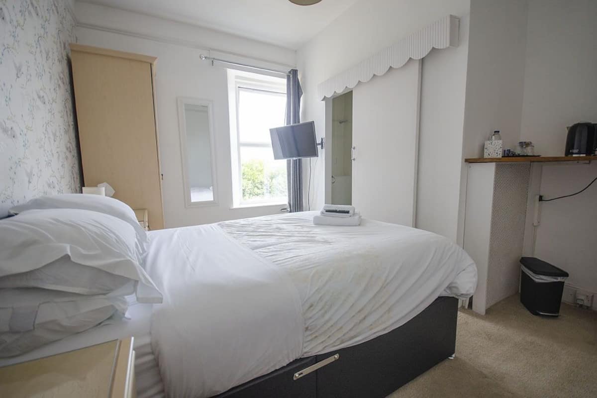 A bedroom with a bed, a TV, a window, and a shelf with items.