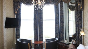 A hotel room with a large window, two chairs, a small table, a television, a kettle, and a lamp. - Headlands Hotel (Llandudno)