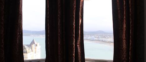 A room with a view of a coastal city through a window with patterned curtains.