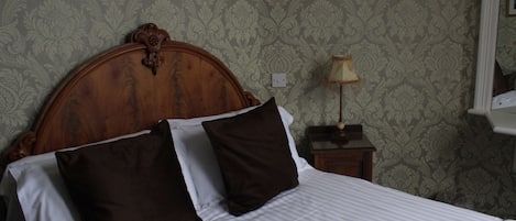 Una cama bien hecha con cabecera de madera, lámpara de noche y un papel tapiz estampado.