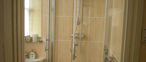 Ducha en esquina con mampara de vidrio, lavamanos y espejo.
