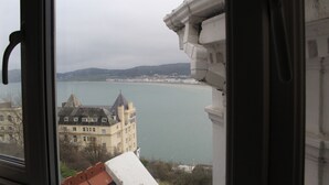 A view of a coastal building with a large window overlooking a body of water and a distant town. - Headlands Hotel (Llandudno)
