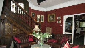 A room with a staircase, leather sofas, a round table with a vase, and framed pictures on the walls. - Headlands Hotel (Llandudno)