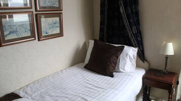Una cama bien hecha con sábanas blancas y almohadas marrones, una mesita de noche con una lámpara y cuadros en la pared.