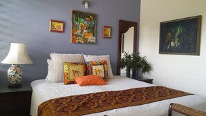 Een slaapkamer met een bed, kussens, een lamp, een spiegel en decoratie aan de muur.