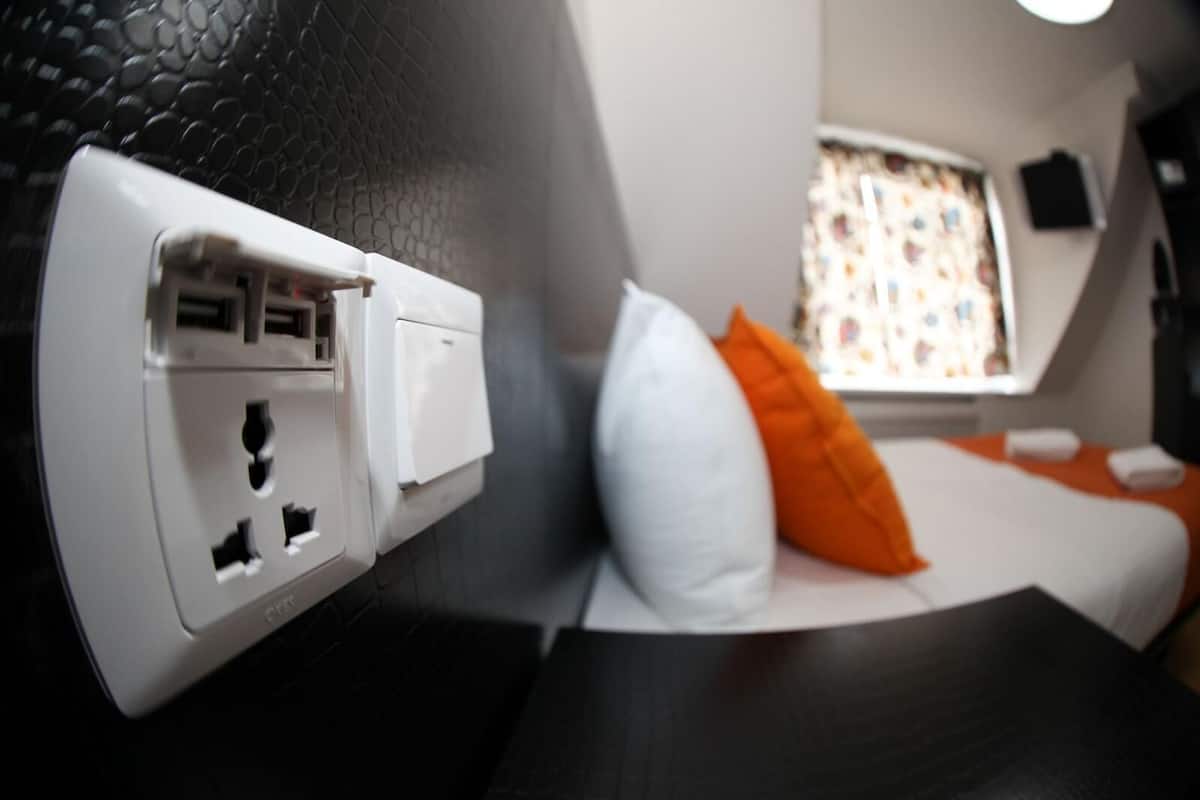 A room with a bed, a window with a view, and an electrical outlet with multiple plugs.