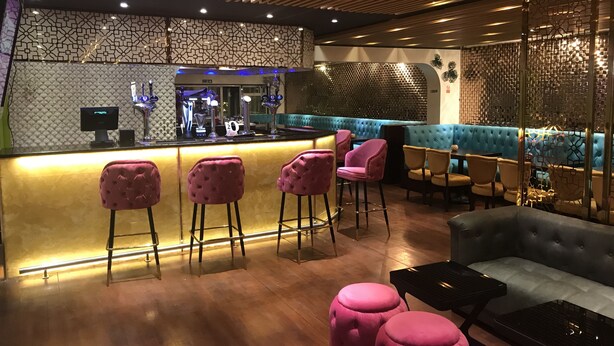 Zona de bar con barra, taburetes rosados y un área de asientos con cojines azules.