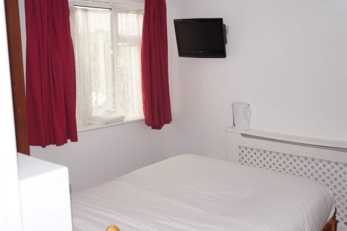 A bedroom with a bed, a television mounted on the wall, and a window with curtains.