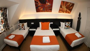 A hotel room with three beds, each with an orange bedspread and white linens, a black headboard, and a wall-mounted artwork above the beds. - Heathrow Inn (Hayes)