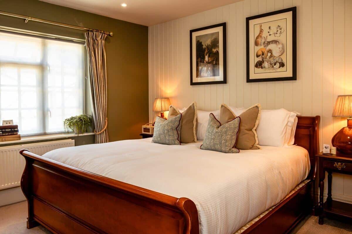 A large bed with a wooden frame, two bedside tables with lamps, and two framed pictures on the wall.