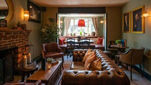 A cozy living room with a fireplace, leather sofa, and a dining area with a table and chairs. - High Corner Inn (Ringwood)