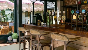 A bar area with wooden chairs, a counter, and a view of the outside through large windows. - High Corner Inn (Ringwood)