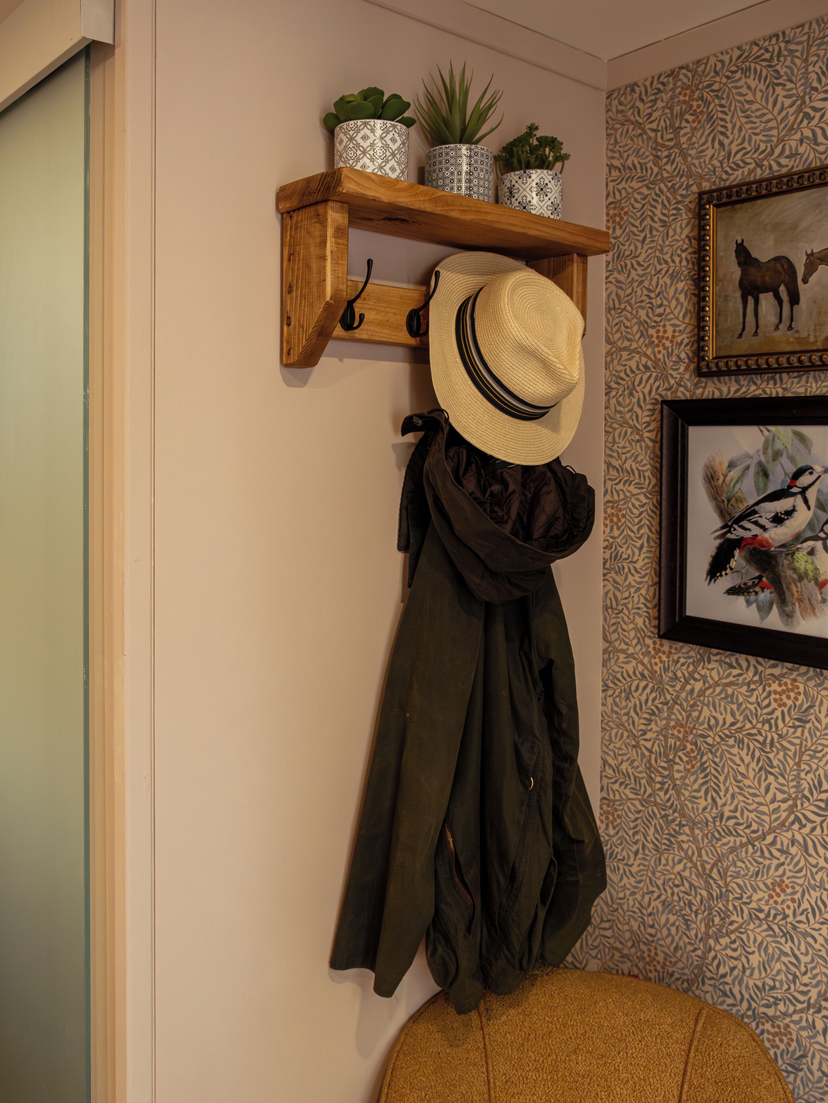 Un perchero de madera con un sombrero y una chaqueta, un estante con macetas decorativas y una pared con diseño que muestra un cuadro de un caballo.