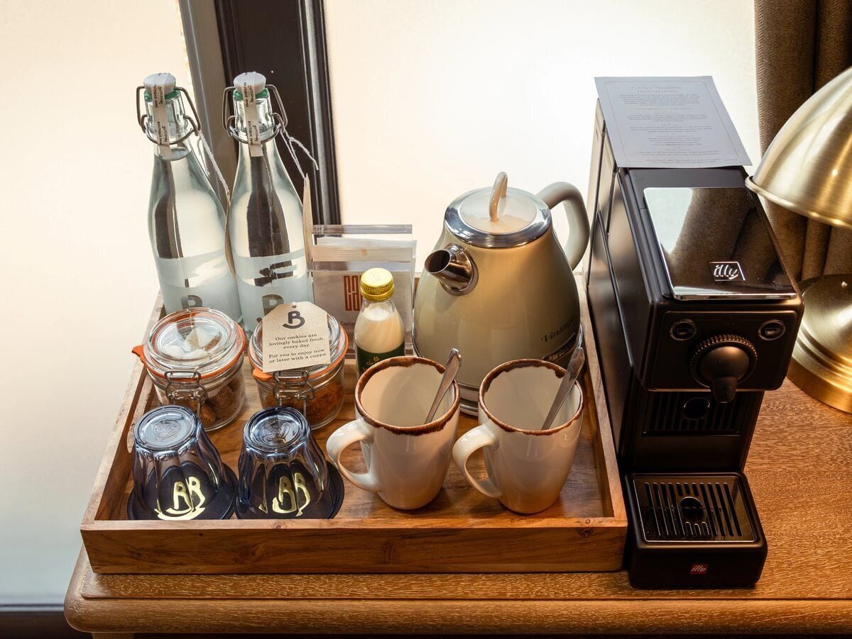 A tray with coffee-making equipment, including a coffee machine, cups, and containers of coffee and creamer.