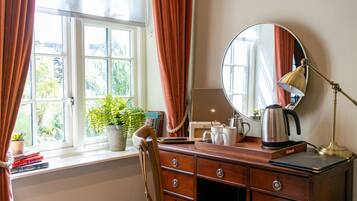Een kamer met een houten dressoir, een spiegel, een bureaulamp, een waterkoker en een raam met gordijnen.